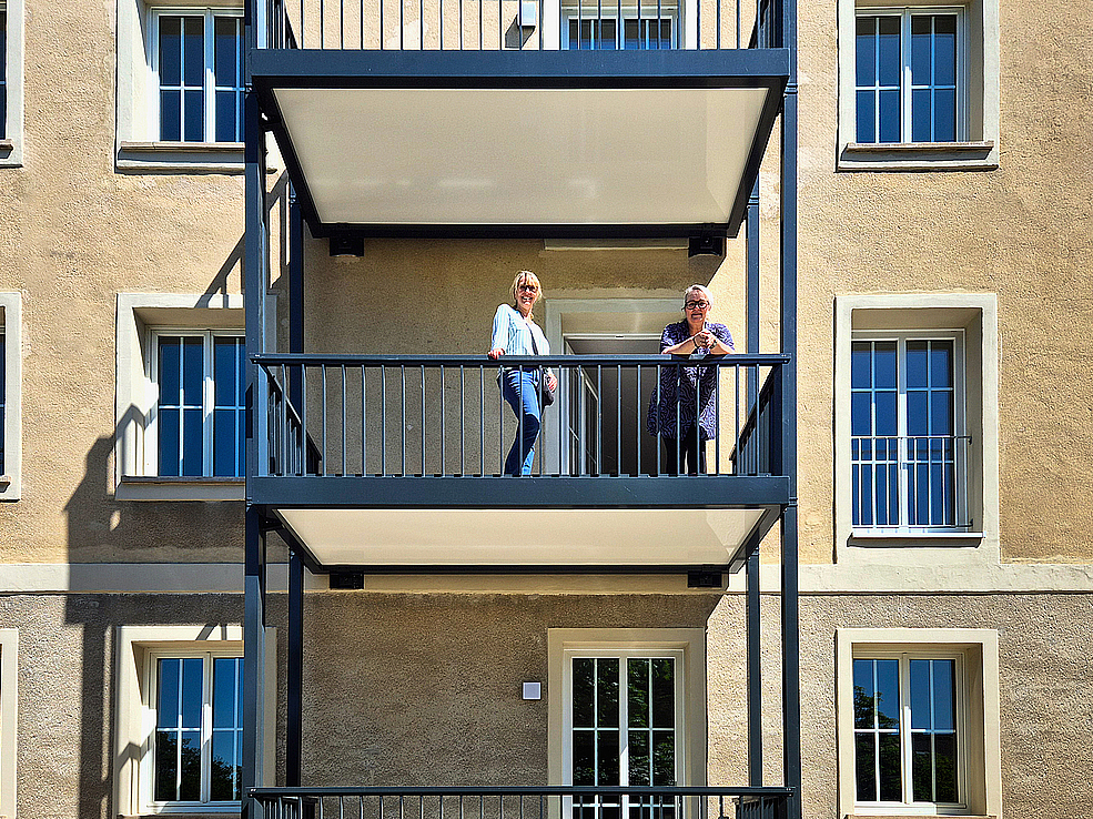 TAG-Marketing-Ansprechpartnerin Susan Nölte steht mit Mieterin Frau Kraul auf dem neu angebauten Balkon im frisch sanierten 1950er-Jahre-Altbau in Dessau-Roßlau.