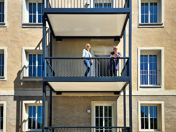 TAG-Marketing-Ansprechpartnerin Susan Nölte steht mit Mieterin Frau Kraul auf dem neu angebauten Balkon im frisch sanierten 1950er-Jahre-Altbau in Dessau-Roßlau.