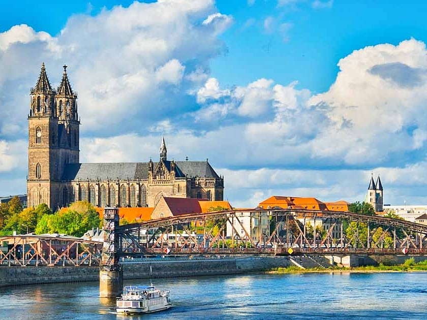 Die Magdeburger Kathedrale vor blauem Himmel mit der Elbe und einer Brücke im Vordergrund