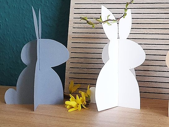 Drei aus Papier gebastelte Osterhasen, dahinter steht ein Schild mit der Aufschrift "Frohe Ostern".
