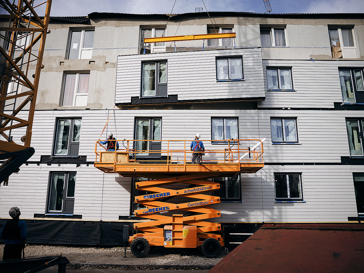 Baufortschitt nach wenigen Tagen: Auf der dritten Etage des Sanierungsobjekts angekommen, sichert ein Arbeiter ein Fassadenmodul gegen Schwenkbewegungen ab.