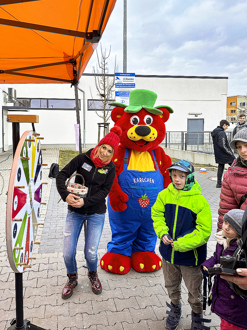 Kinder stehen am Glücksrad und das Karls Maskottchen sieht zu.