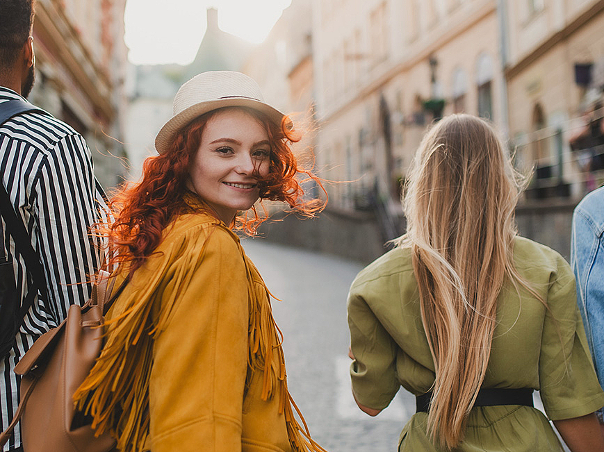 Frau ist mit ihren Freunden in der sinnigen Innenstadt unterwegs und dreht sich um und lächelt in die Kamera