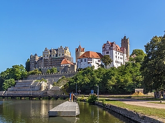 Das große Schloss Bernburg ist im Hintergrund zu sehen und davor fließt der Fluss Saale entlang