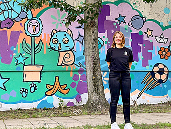 Das Bild zeigt Jolina Seide vor der Hauswand, die mit Graffiti besprüht ist