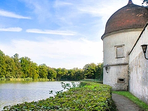Ein entspannter Spaziergang bei schönem Wetter im Schlosspark Hermsdorf entlang der historischen Schlossmauer mit malerischen Türmchen und einem See