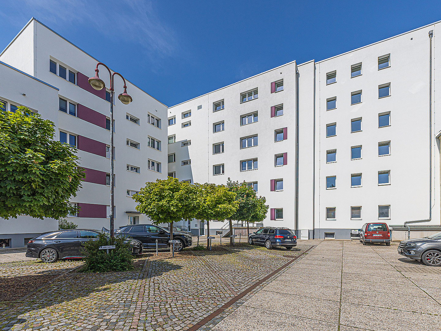 Innenhofansicht sanierter Mehrfamilienhäuser in der Johannisstraße in Döbeln mit gepflasterter Fläche, Bäumen und geparkten Autos bei blauem Himmel