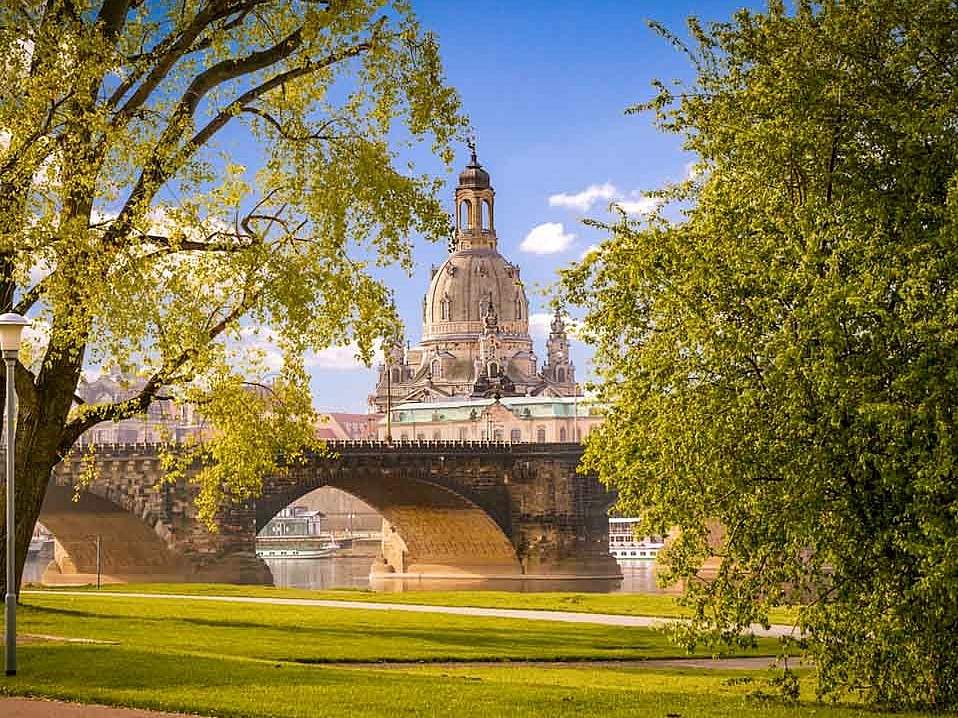 Grünfläche im Vordergrund dahinter das die große Brücke über die Elbe und die Frauenkirche bei Sonnenschein in Dresden