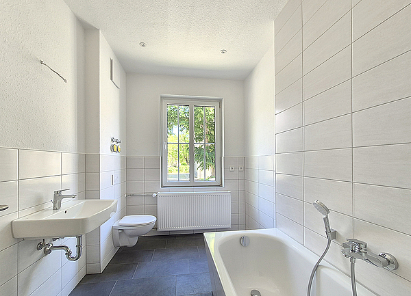 Grundsaniertes Bad mit Badewanne, hängendem Toilettenbecken und modernem Waschbecken und einem großen Fenster mit Fensterkreuzen in einer Altbauwohnung aus den 1950er Jahren im Wohnquartier Biethe in Dessau-Roßlau