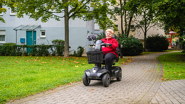 Eine Frau fährt mit einem Elektro-Sitzroller durch ein Wohngebiet.  