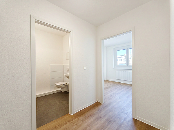 Blick in den frisch modernisierten Flur einer Wohnung in der Otto-Nagel-Straße mit Zugang zum neuen Badezimmer und einem hellen Zimmer mit Fenster und Holzboden.