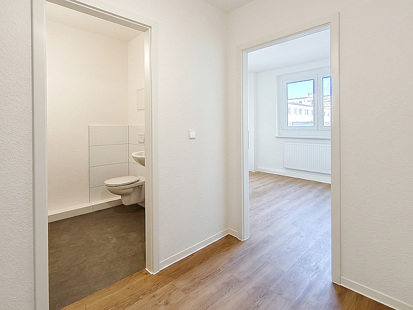 Blick in den frisch modernisierten Flur einer Wohnung in der Otto-Nagel-Straße mit Zugang zum neuen Badezimmer und einem hellen Zimmer mit Fenster und Holzboden.
