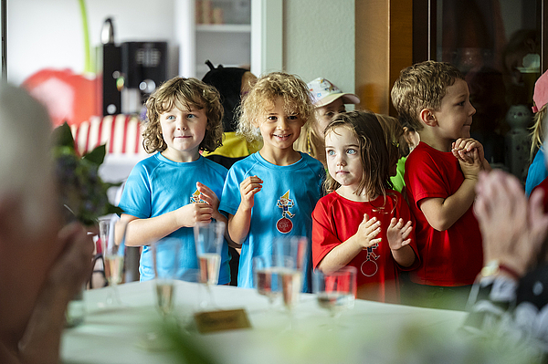 Kinder des Kindergartens „Pfiffikus“ stehen in bunten T-Shirts vor den Gästen und gestalten mit ihrer Darbietung das Rahmenprogramm der Jubiläumsfeier von TAG Wohnen und dem Pflegedienst Kraft.