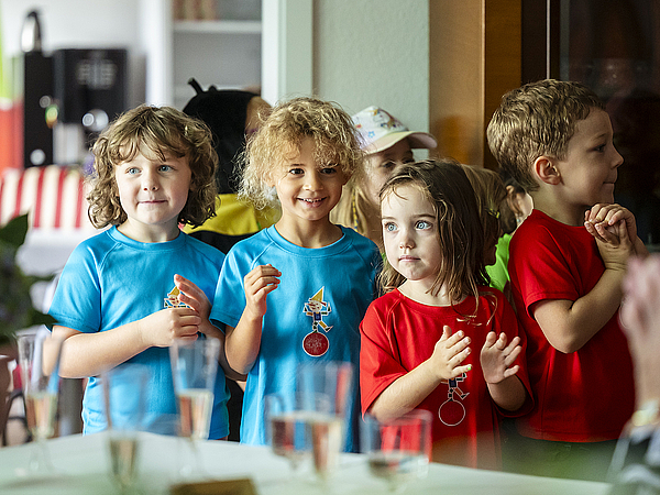 Kinder des Kindergartens „Pfiffikus“ stehen in bunten T-Shirts vor den Gästen und gestalten mit ihrer Darbietung das Rahmenprogramm der Jubiläumsfeier von TAG Wohnen und dem Pflegedienst Kraft.