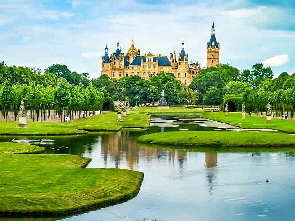 Die Schlossinsel mit Wasser, einem grünen Park und dem Schweriner Schloss im Hintergrund in Schwerin