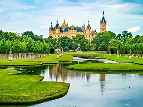 Die Schlossinsel mit Wasser, einem grünen Park und dem Schweriner Schloss im Hintergrund in Schwerin