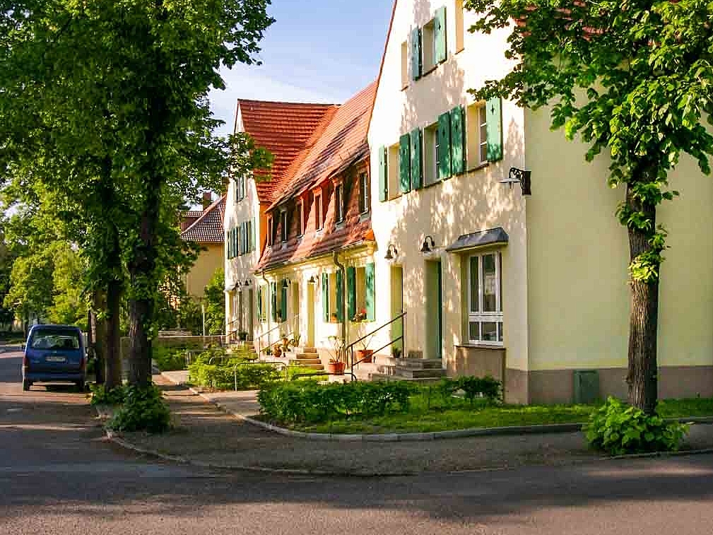 Kleines gelbes Mehrfamilienhaus mit grünen Fensterläden umgeben von Bäumen in der Rosa-Luxemberg-Straße in Lauta.