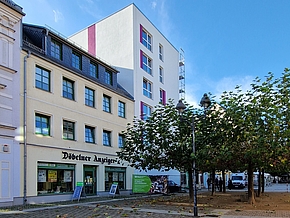 Auf der linken Seiter stehen Häuser in rosa, gelb und weiß und auf der rechten Seite sind ein paar bäume bepflanzt