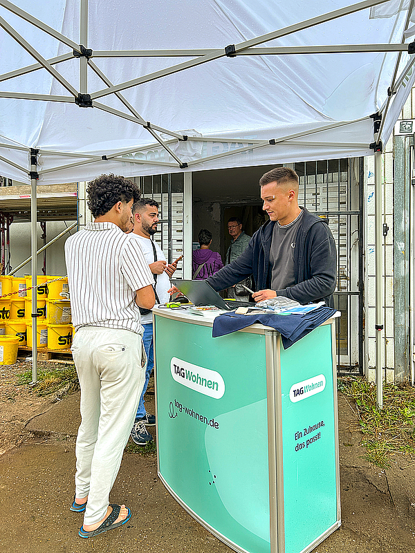 Ein Mitarbeiter von TAG Wohnen berät zwei Interessenten am Infostand vor dem Eingang des modernisierten Zehngeschossers in der Otto-Nagel-Straße im Magdeburger Stadtteil Kannenstieg.