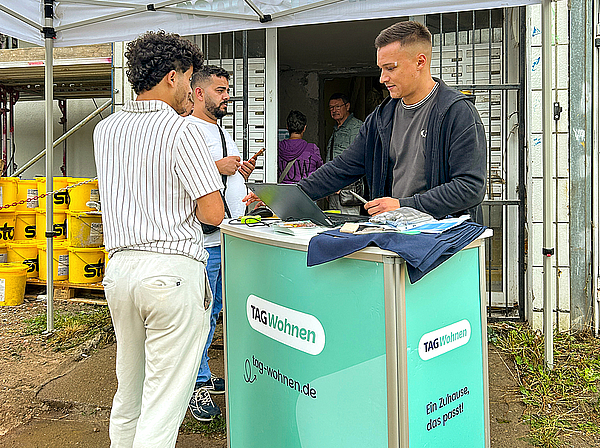 Ein Mitarbeiter von TAG Wohnen berät zwei Interessenten am Infostand vor dem Eingang des modernisierten Zehngeschossers in der Otto-Nagel-Straße im Magdeburger Stadtteil Kannenstieg.