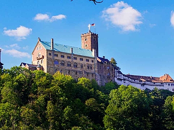 Die imposante mittelalterliche Wartburg thront majestätisch über grünen Bäumen vor einem strahlend blauen Himmel