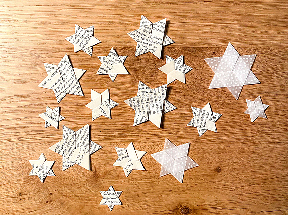 Aus Papier gefaltete Sterne liegen auf einem Holztisch ausgebreitet.