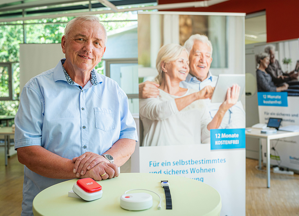 Ein Mann steht vor einem Messestand und präsentiert die Hilfsmittel des Assistenzsystems "BeHome".