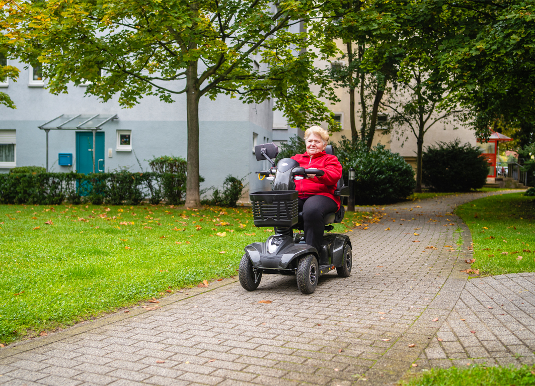 Eine Frau fährt mit einem Elektro-Sitzroller durch ein Wohngebiet.  