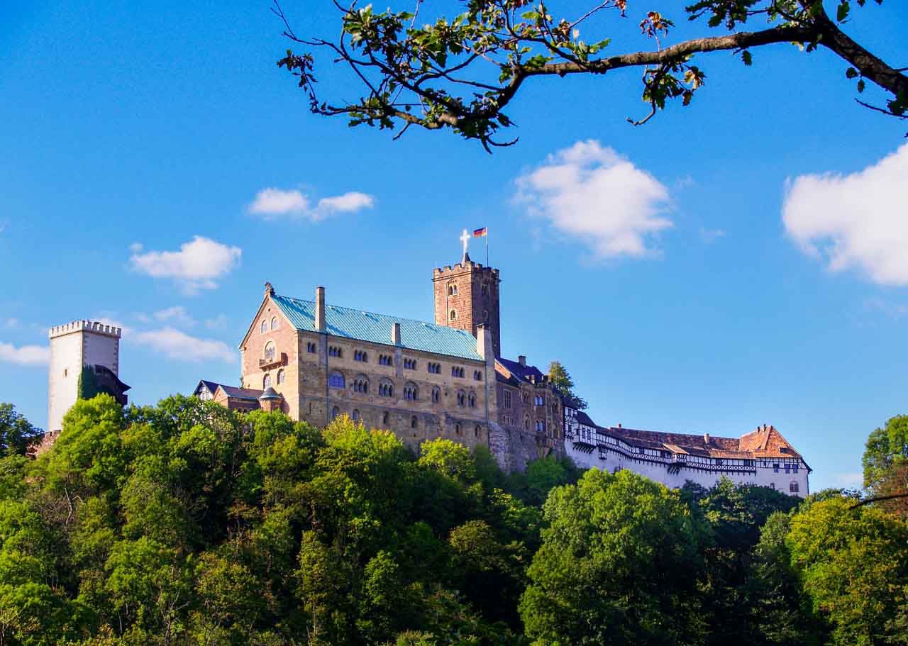 Die imposante mittelalterliche Wartburg thront majestätisch über grünen Bäumen vor einem strahlend blauen Himmel