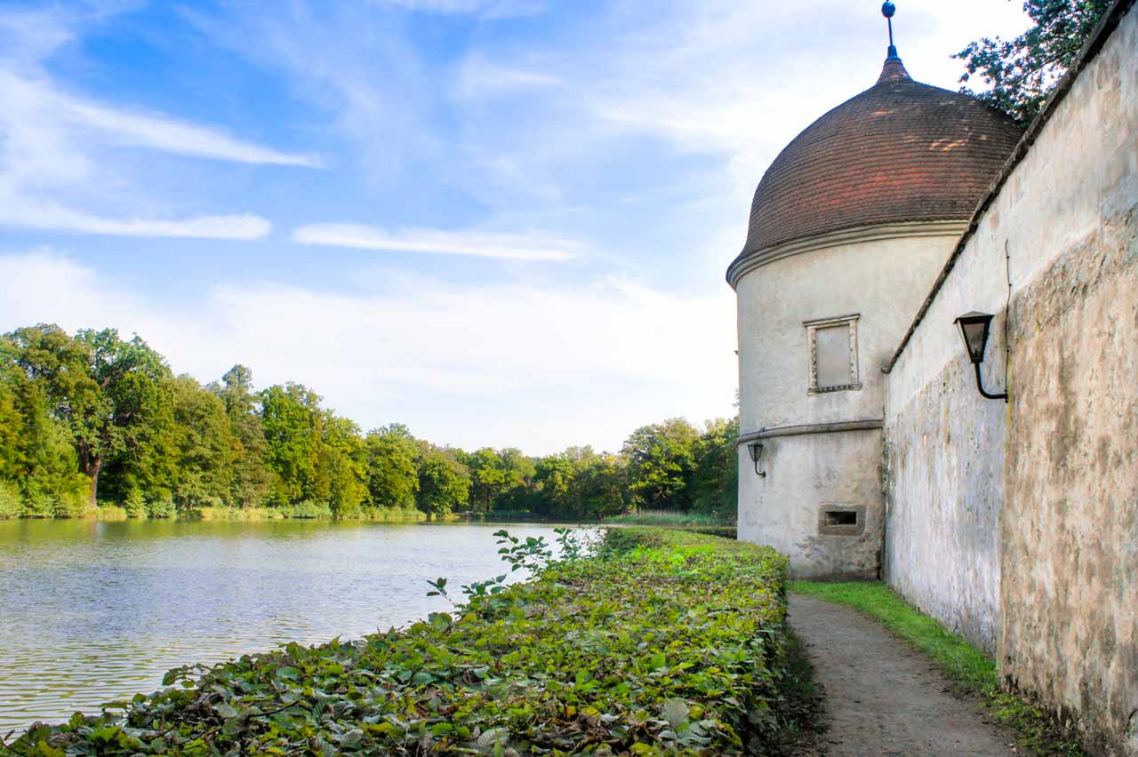 Ein entspannter Spaziergang bei schönem Wetter im Schlosspark Hermsdorf entlang der historischen Schlossmauer mit malerischen Türmchen und einem See